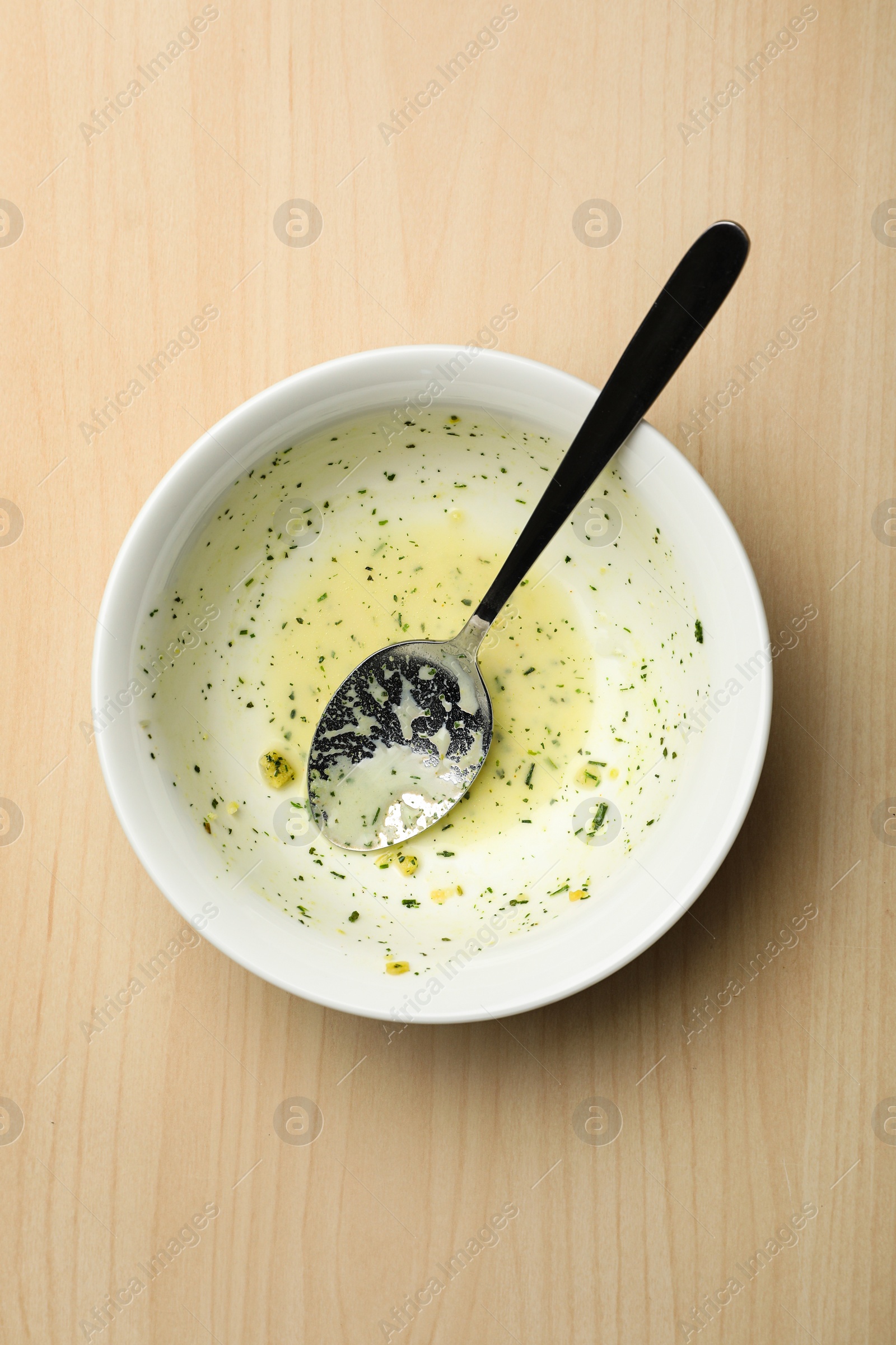 Photo of Dirty bowl with food leftovers and spoon on wooden background, top view