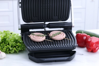 Photo of Electric grill with homemade sausages and rosemary on white table