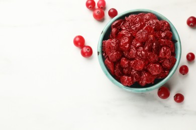Photo of Tasty dried cranberries in bowl and fresh ones on white table, top view. Space for text