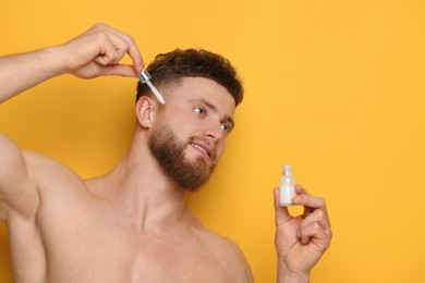 Photo of Handsome man applying serum onto his face on orange background