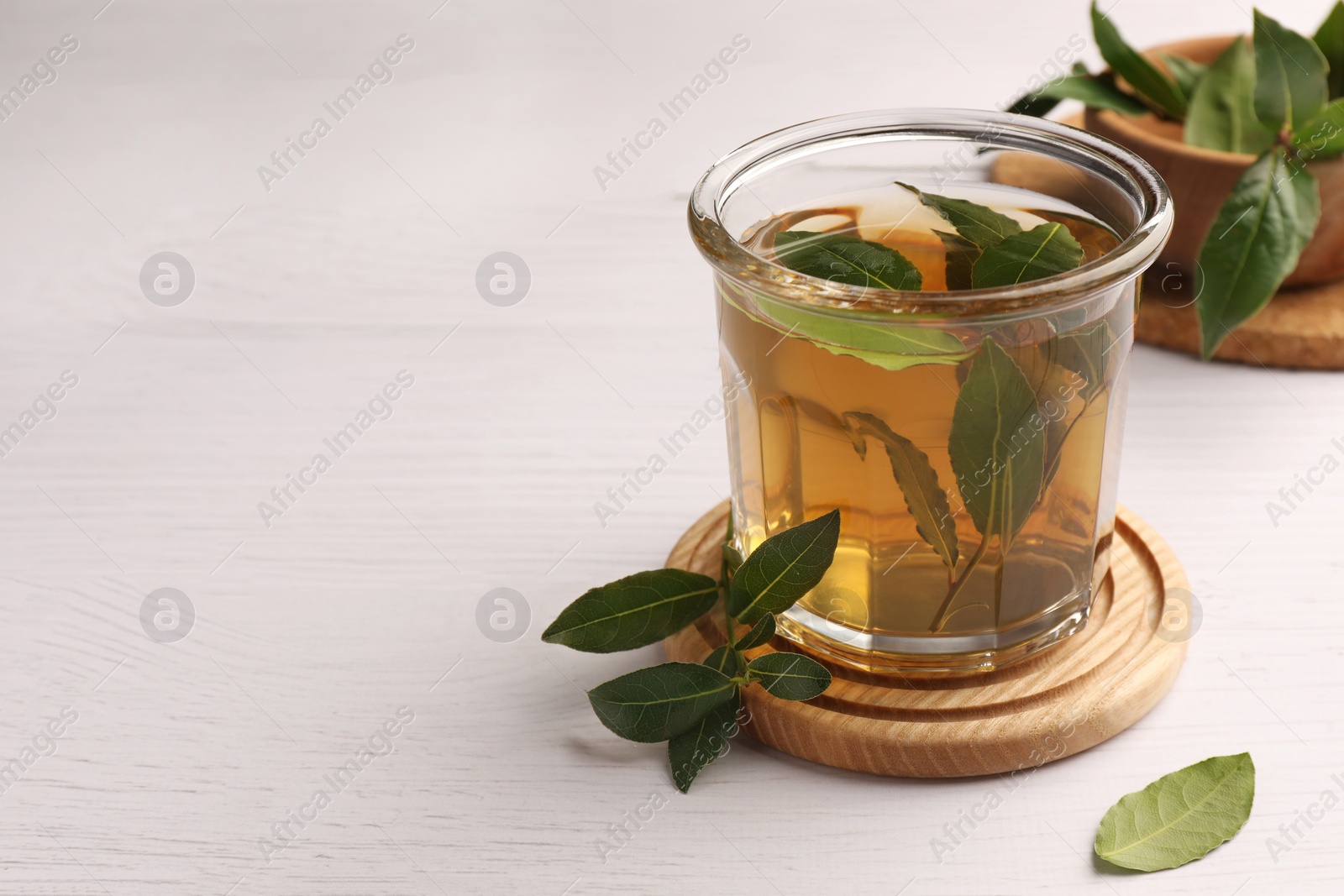 Photo of Cup of freshly brewed tea with bay leaves on white wooden table, closeup. Space for text