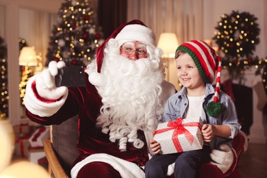 Photo of Santa Claus and little boy taking selfie in room decorated for Christmas