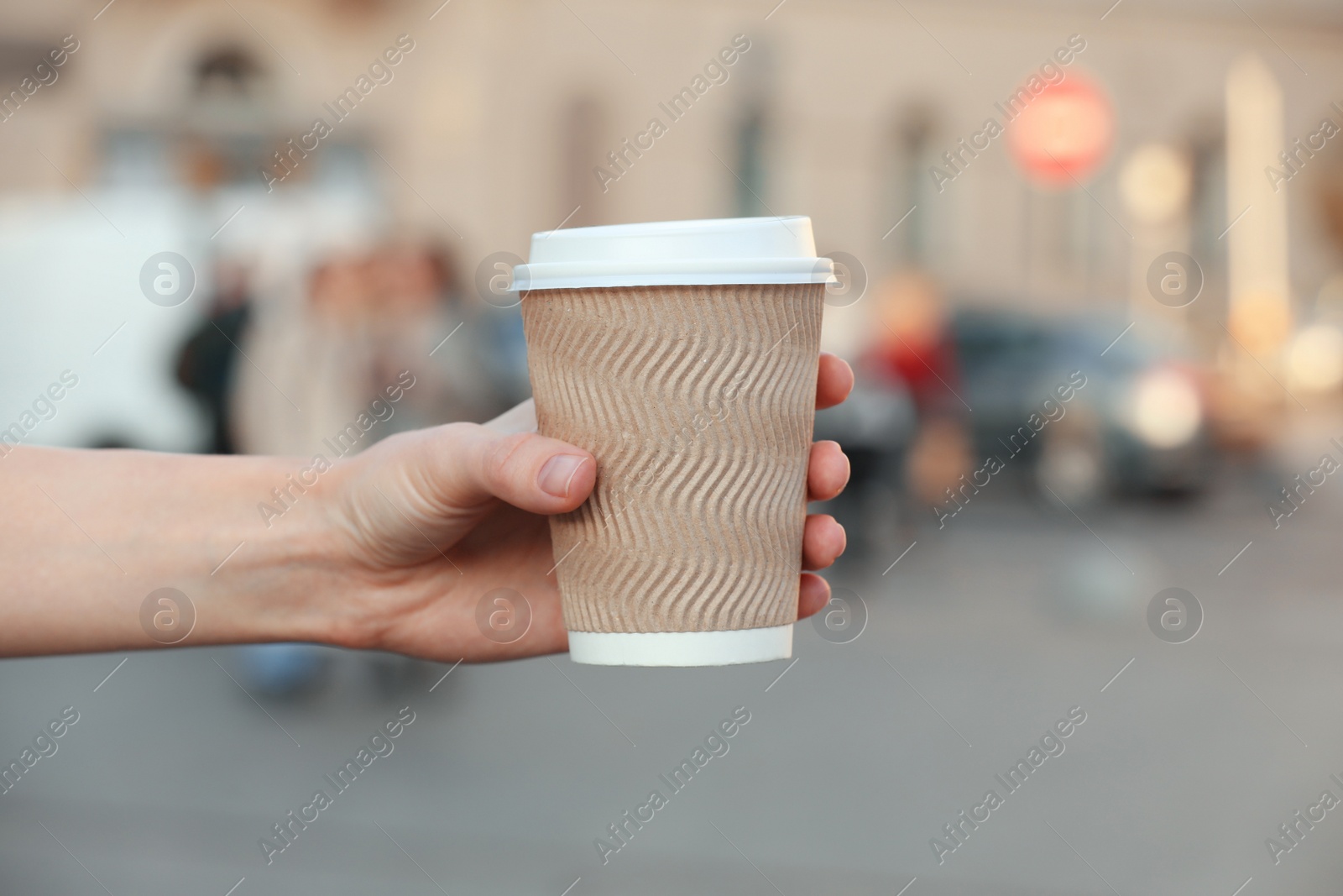 Photo of Woman holding paper takeaway cup on city street, closeup. Coffee to go