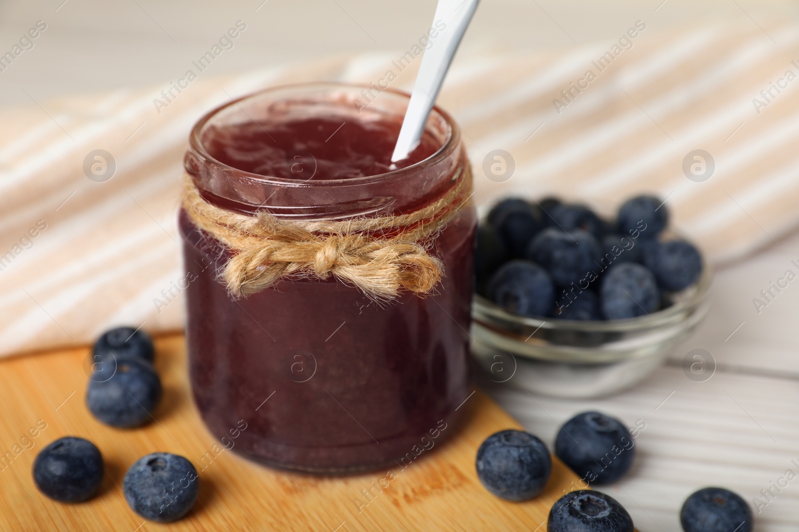 Photo of Jar of delicious blueberry jam and fresh berries on white wooden table, closeup