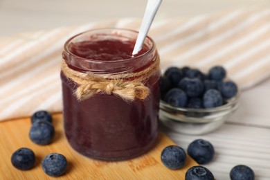 Photo of Jar of delicious blueberry jam and fresh berries on white wooden table, closeup