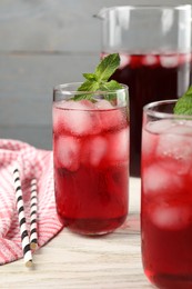 Photo of Delicious iced hibiscus tea with mint and straws on white wooden table