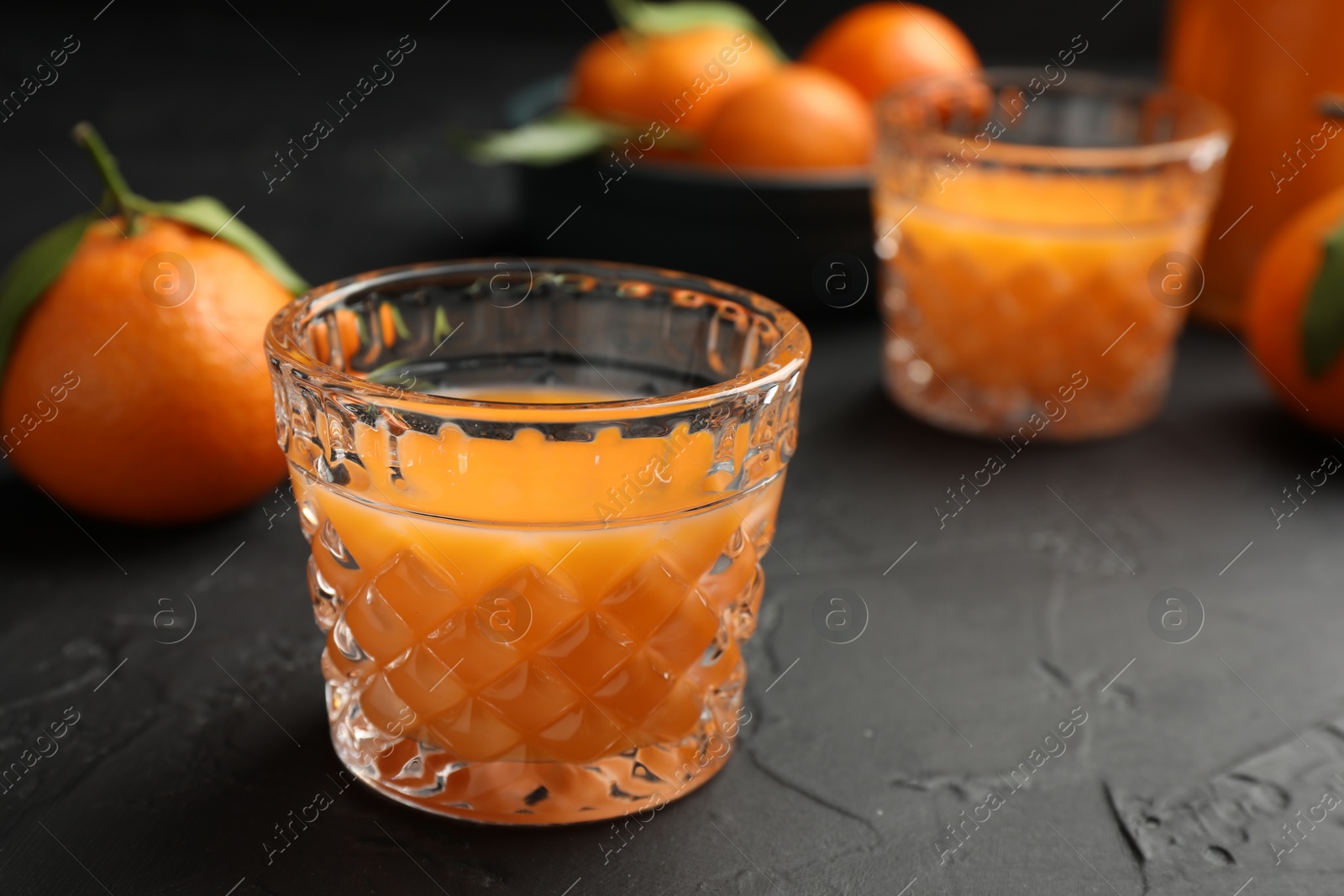 Photo of Tasty tangerine liqueur in glasses and fresh citrus fruits on black textured table. Space for text