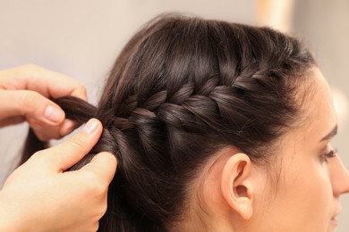 Photo of Professional stylist braiding client's hair on blurred background, closeup