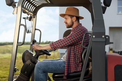 Photo of Farmer in hat driving loader outdoors. Agriculture equipment