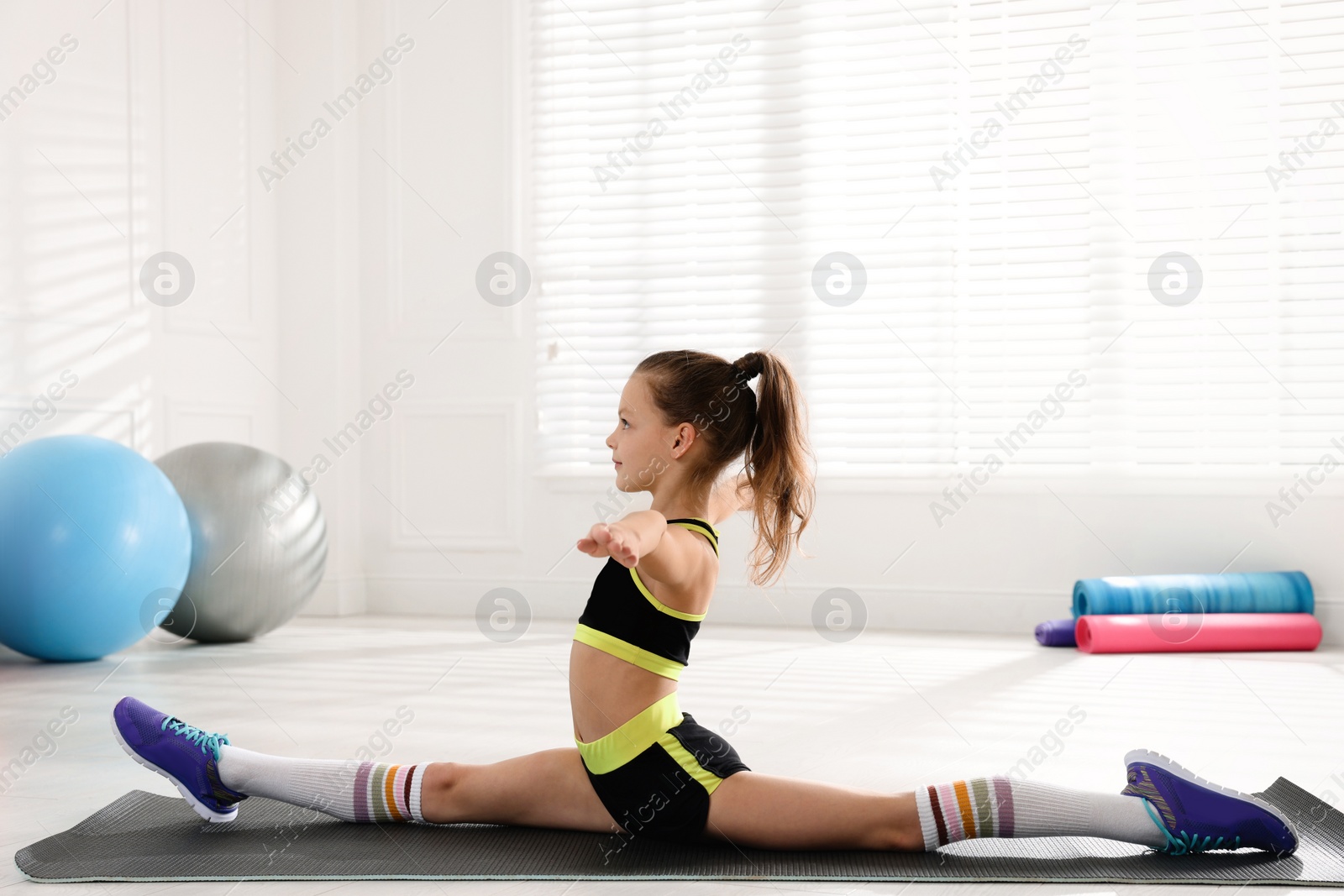 Photo of Cute little girl doing gymnastic exercise indoors. Front split