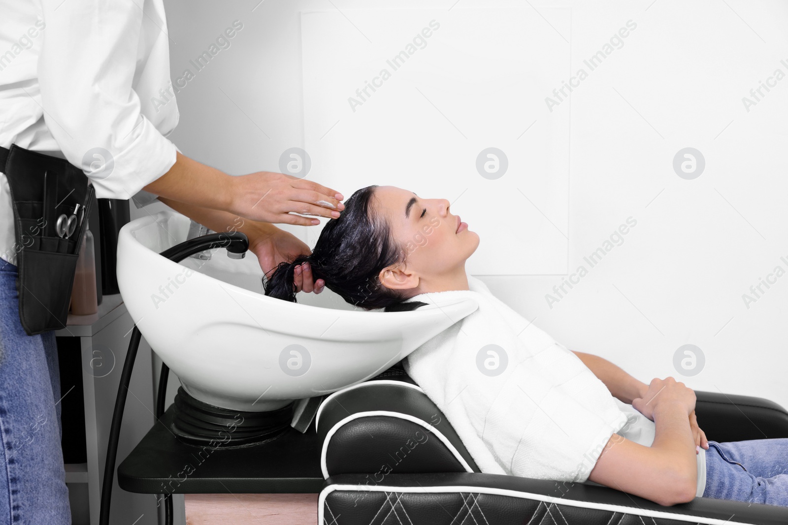 Photo of Professional hairdresser washing woman's hair in beauty salon, closeup