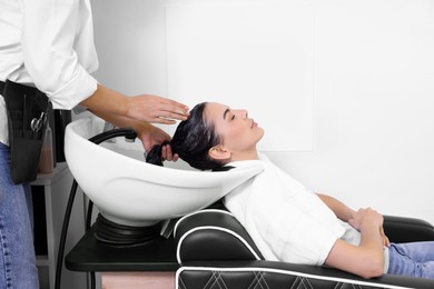 Photo of Professional hairdresser washing woman's hair in beauty salon, closeup