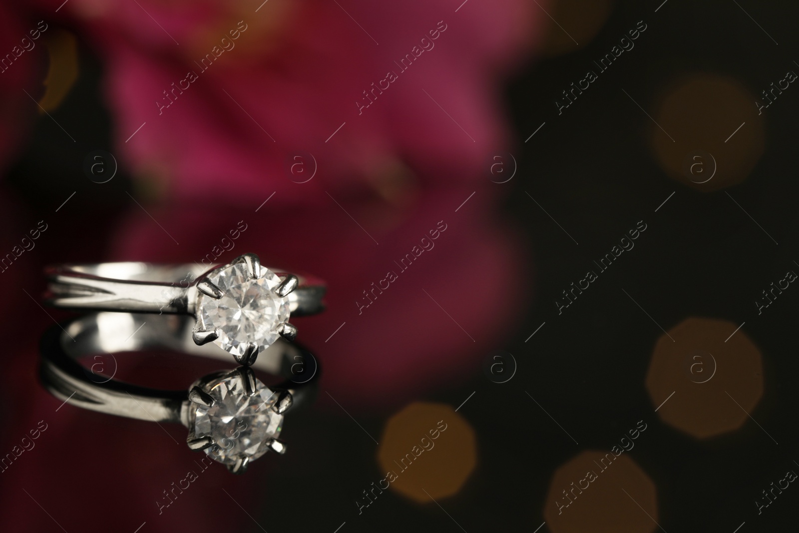 Photo of Beautiful engagement ring against blurred festive lights, closeup. Space for text