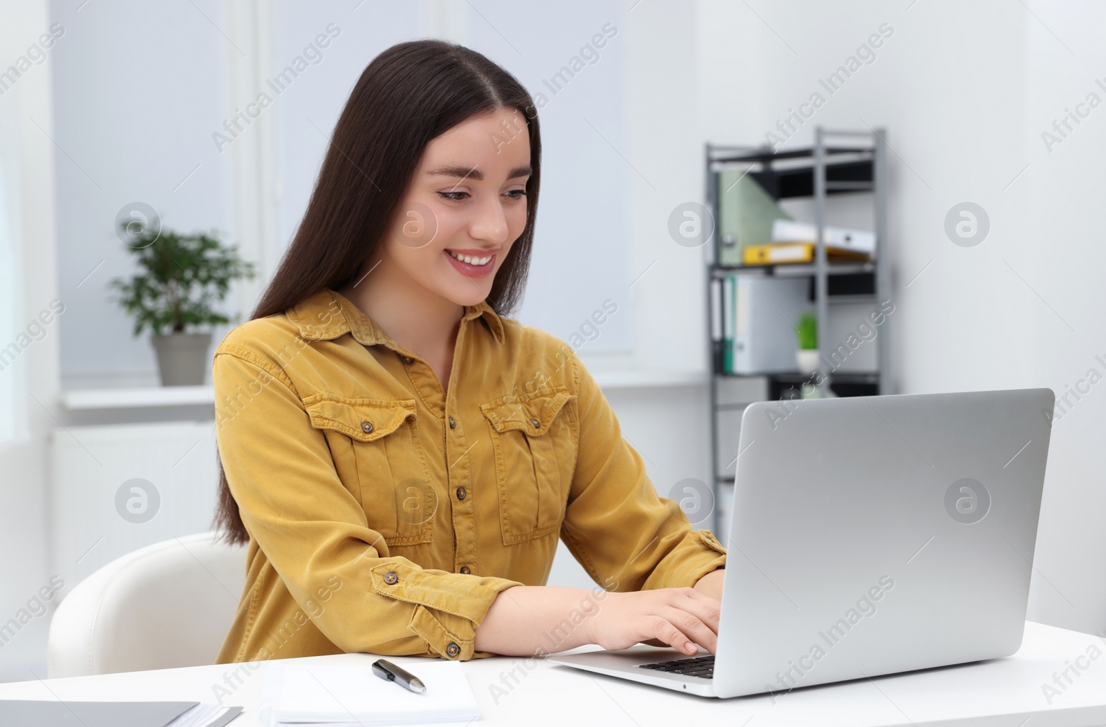 Photo of Young female intern working with laptop at table in office