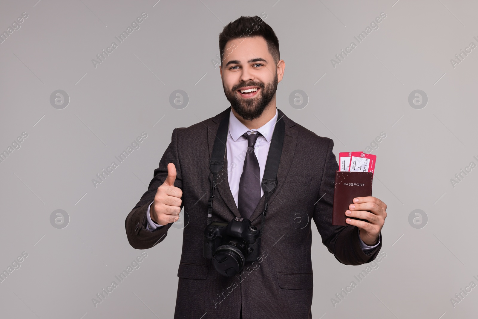Photo of Happy businessman with passport, tickets and camera showing thumb up on grey background