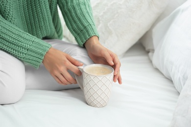 Photo of Young woman in warm sweater with hot drink on bed at home, closeup. Space for text