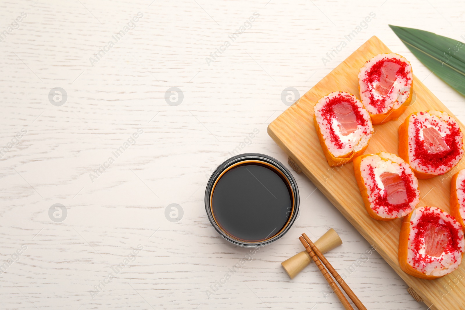 Photo of Delicious sushi rolls with salmon, chopsticks and soy sauce on white wooden table, flat lay. Space for text