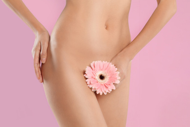 Photo of Woman with flower showing smooth skin after Brazilian bikini epilation on pink background, closeup. Body care concept