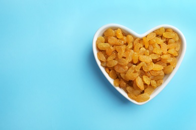 Bowl of raisins on color background, top view with space for text. Dried fruit as healthy snack