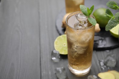 Photo of Glass of tasty ginger ale with ice cubes and ingredients on grey wooden table, closeup. Space for text
