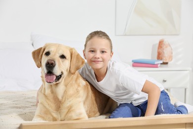Photo of Cute child with her Labrador Retriever on bed at home. Adorable pet