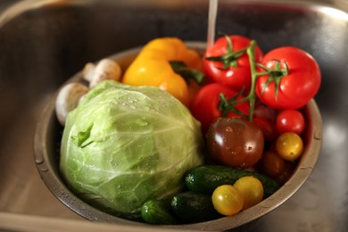 Photo of Washing different vegetables with tap water in metal colander inside sink, closeup