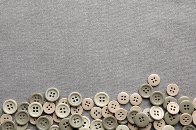 Many plastic sewing buttons on grey fabric, flat lay. Space for text