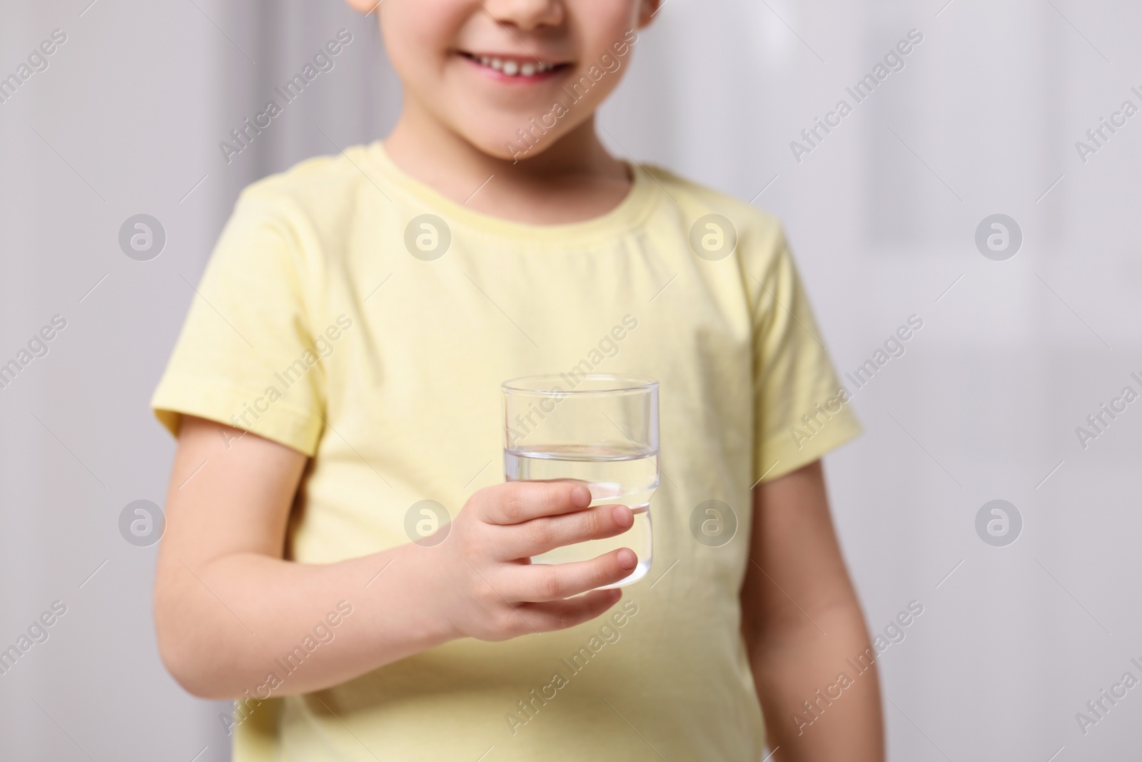 Photo of Little girl holding glass of fresh water indoors, closeup