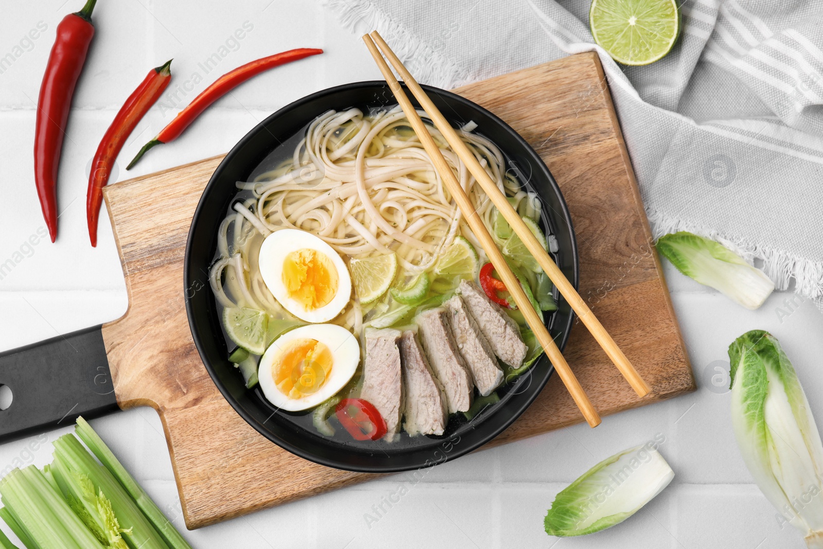 Photo of Bowl of delicious rice noodle soup with meat and egg on white tiled table, flat lay