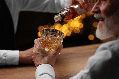 Bartender pouring whiskey in glass for customer at bar counter, closeup