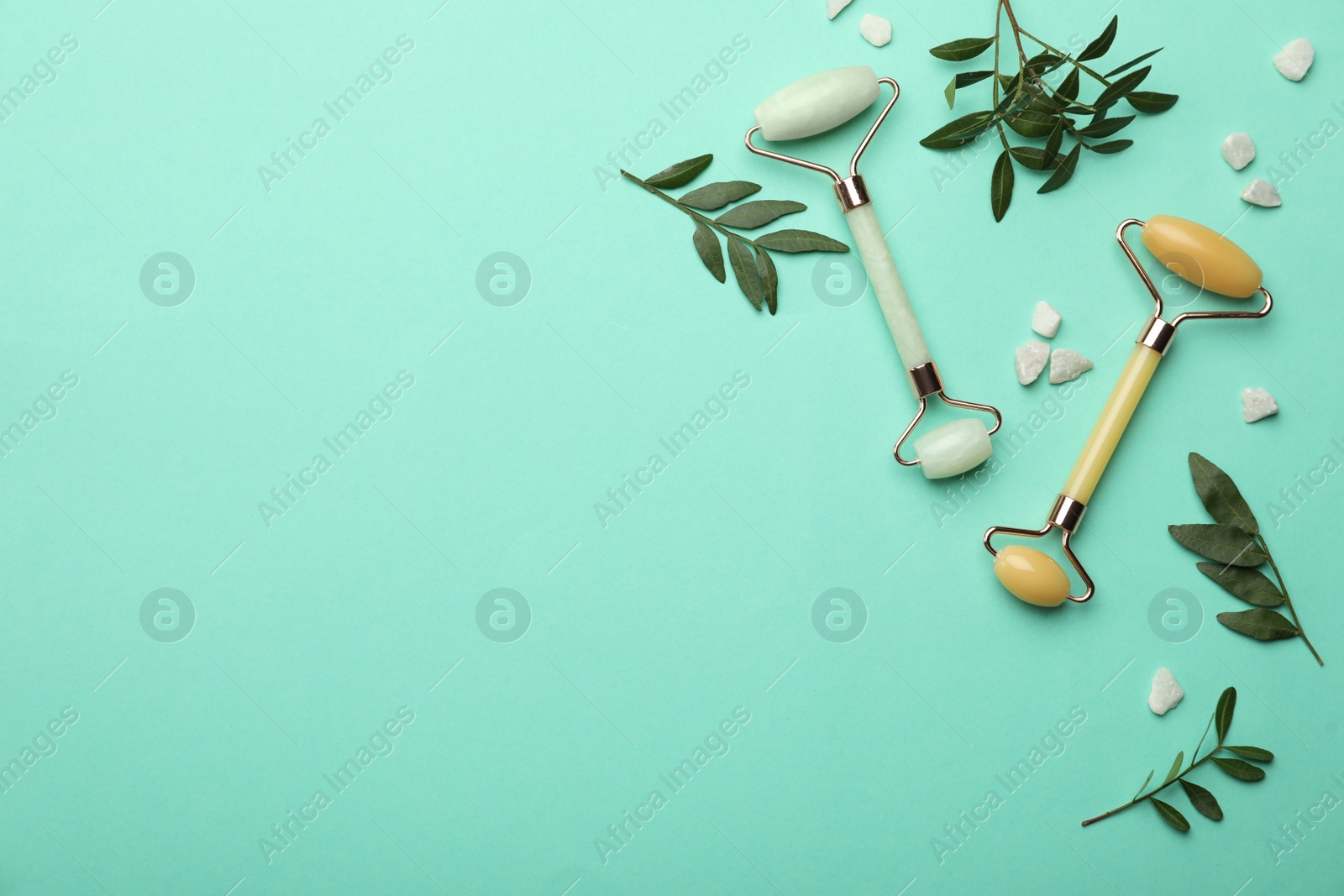 Photo of Natural face rollers and leaves on turquoise background, flat lay. Space for text