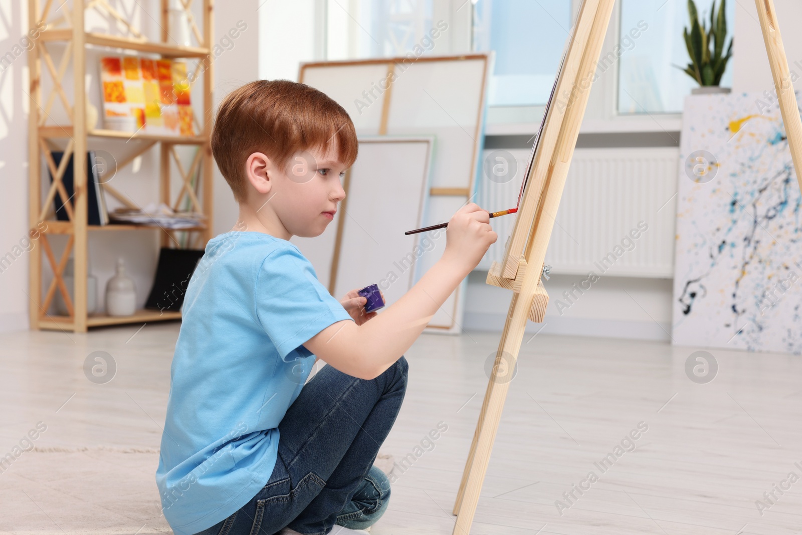 Photo of Little boy painting in studio. Using easel to hold canvas