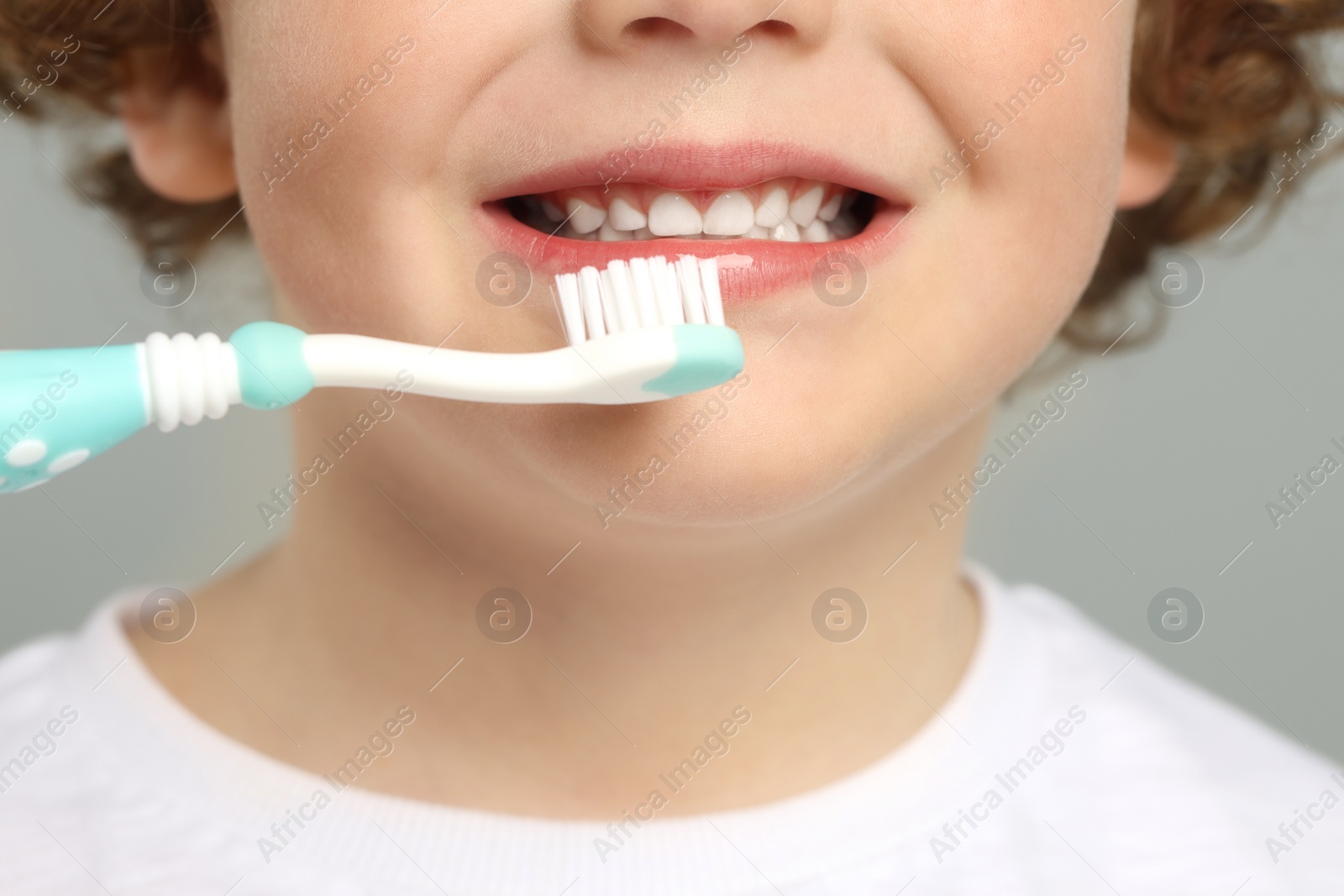 Photo of Cute little boy brushing his teeth with plastic toothbrush on light grey background, closeup