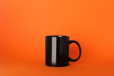 Photo of Blank black ceramic mug on orange background