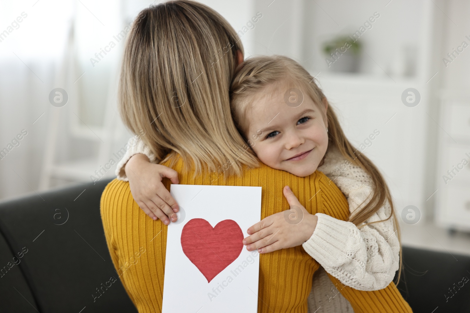 Photo of Little daughter congratulating her mom with greeting card at home. Happy Mother's Day