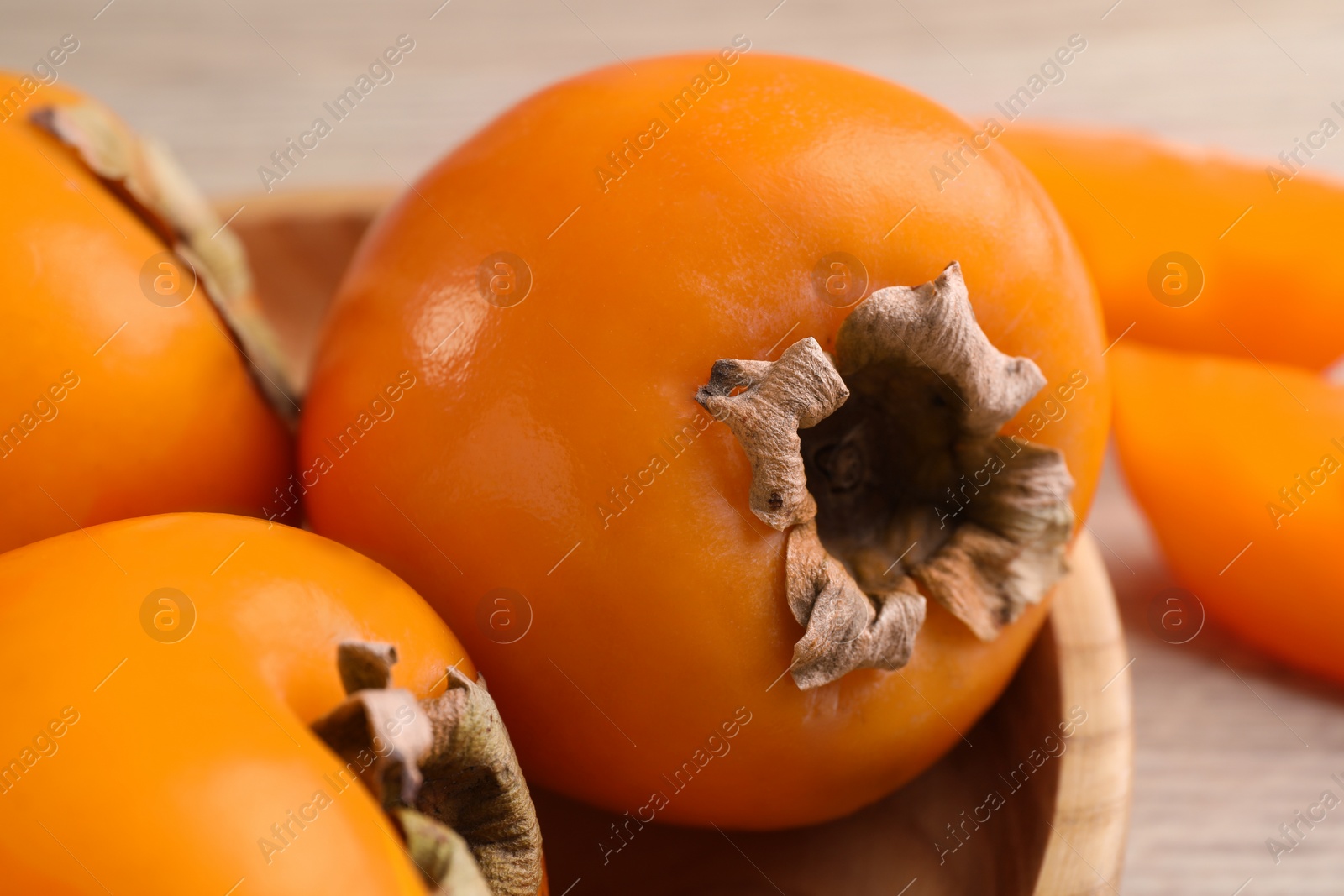 Photo of Delicious ripe persimmons in bowl on table, closeup