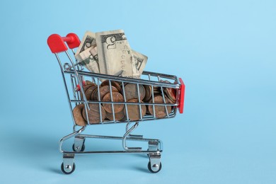 Small metal shopping carts with money on light blue background, space for text