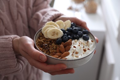 Woman holding bowl of tasty granola indoors, closeup