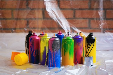 Photo of Used cans of spray paints on floor indoors. Graffiti supplies