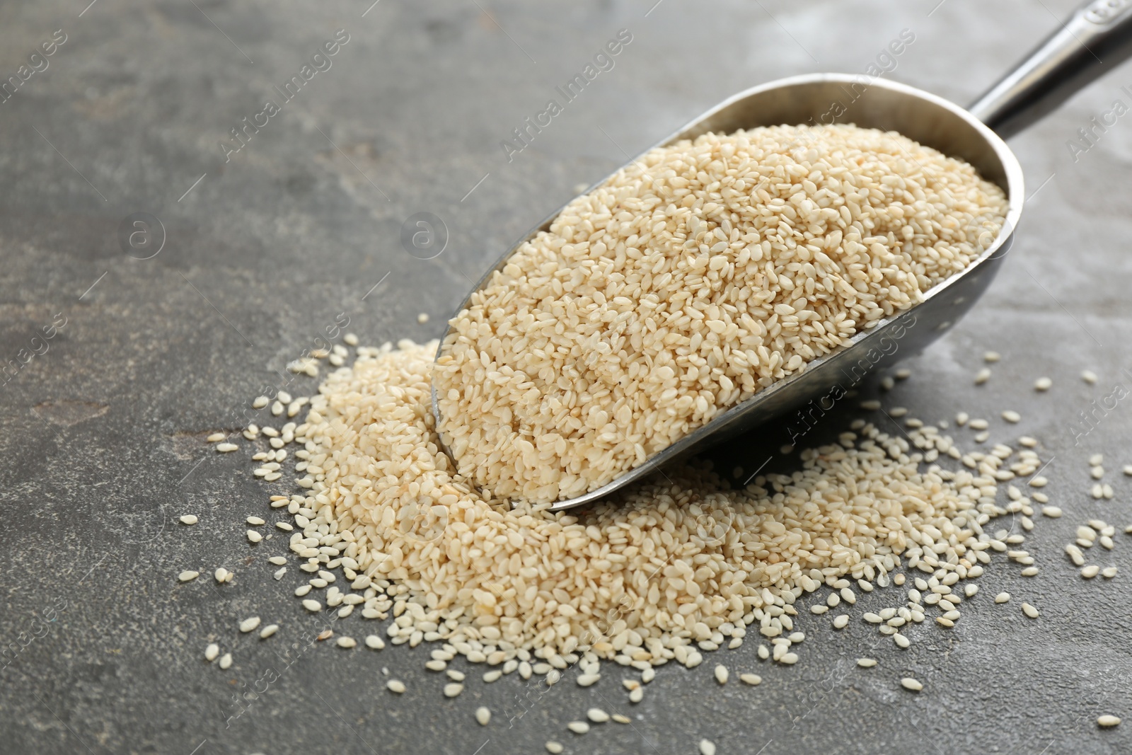 Photo of Metal scoop with white sesame seeds on grey table