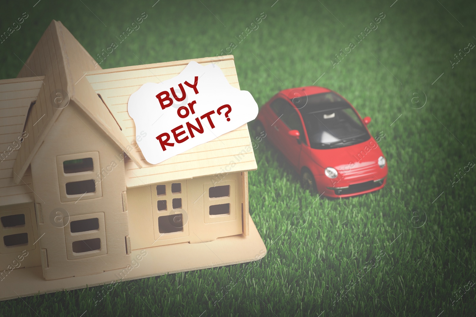 Image of Model of house with card Buy Or Rent near toy car on green grass