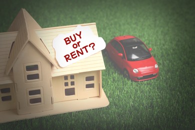 Model of house with card Buy Or Rent near toy car on green grass