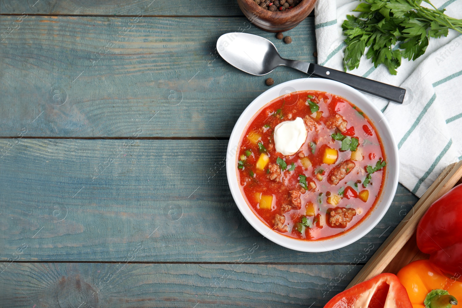 Photo of Bowl of delicious stuffed pepper soup on light blue wooden table, flat lay. Space for text