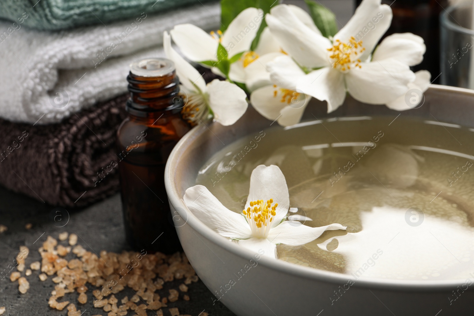 Photo of Beautiful spa composition with jasmine essential oil and fresh flowers on grey table, closeup