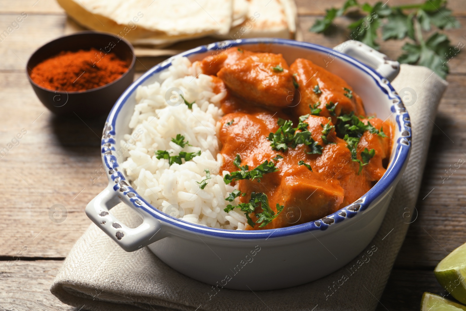 Photo of Delicious butter chicken with rice in bowl served on wooden table