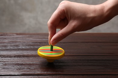 Photo of Woman playing with bright spinning top at wooden table, closeup