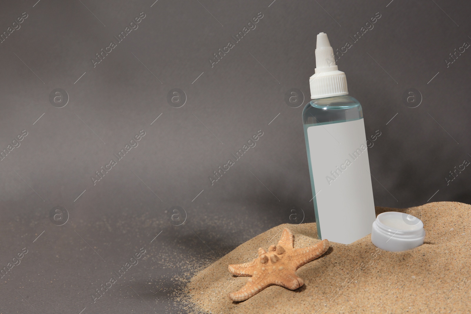 Photo of Cosmetic products and starfish on sand against grey background. Space for text