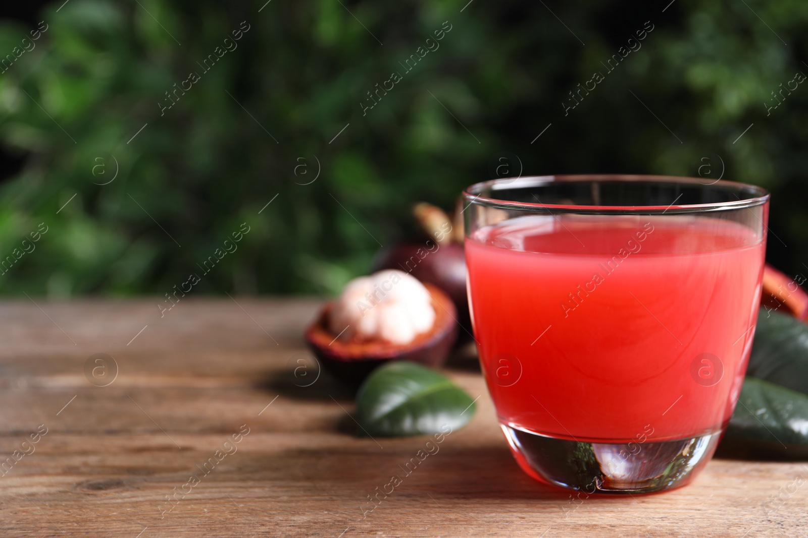 Photo of Delicious mangosteen juice in glass on wooden table. Space for text