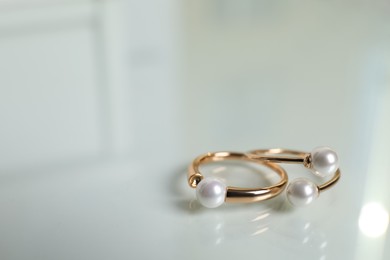 Photo of Elegant golden rings with pearls on white table, closeup. Space for text