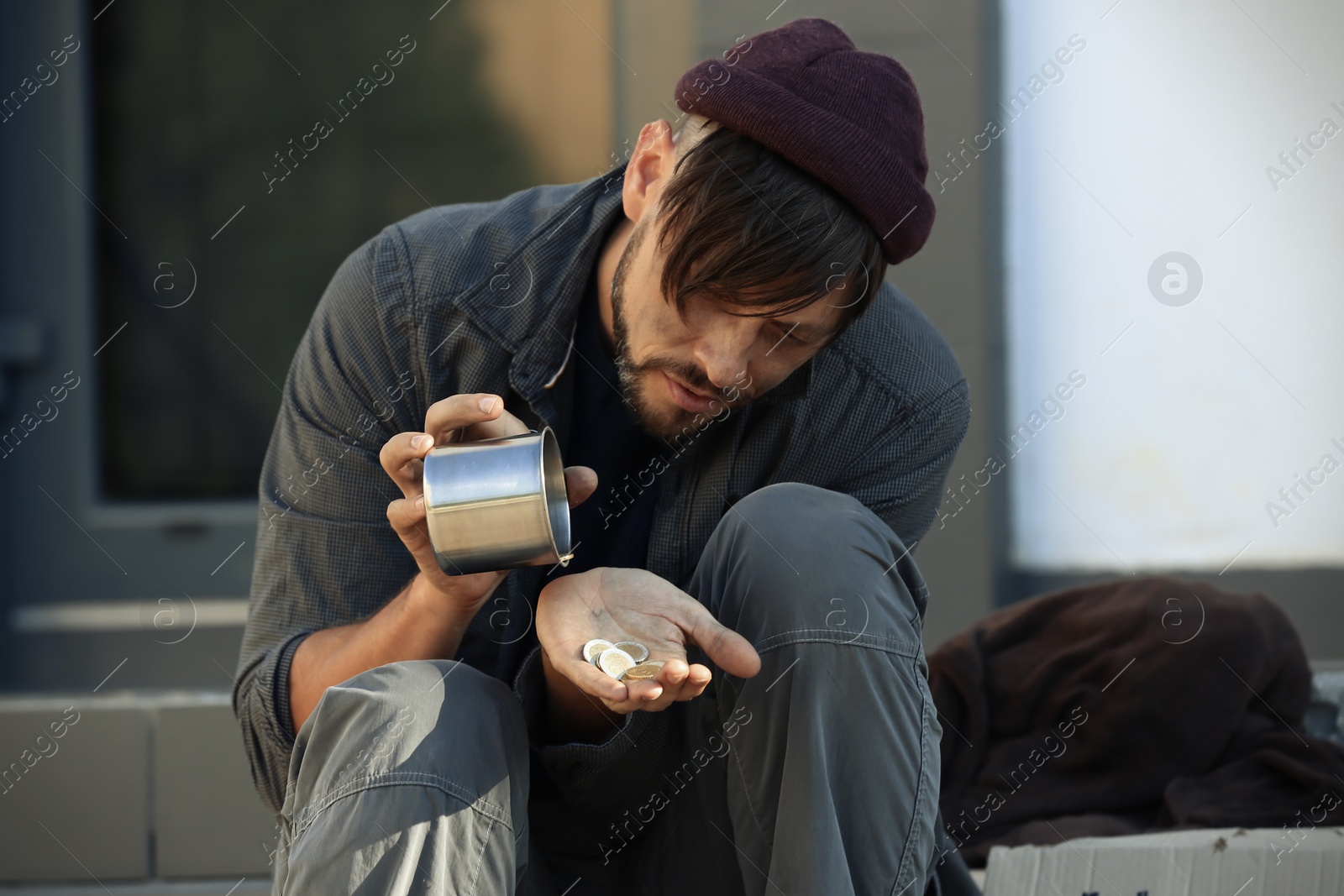 Photo of Poor man with mug counting coins on city street